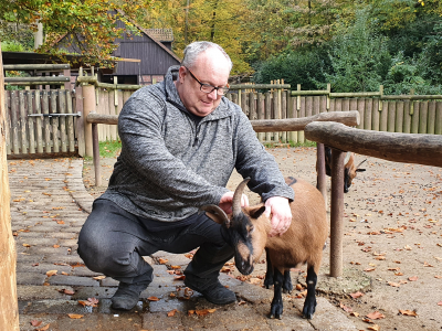 älterer Mann kniet neben einer Ziege